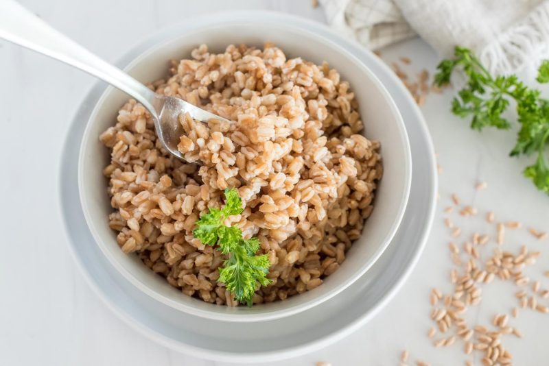 Instant Pot farro in a white bowl with a fresh sprig of parsley.